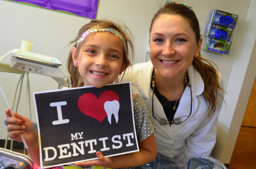 A dentist smiles in a photo with a young patient holding a sign that reads, "I love my dentist".