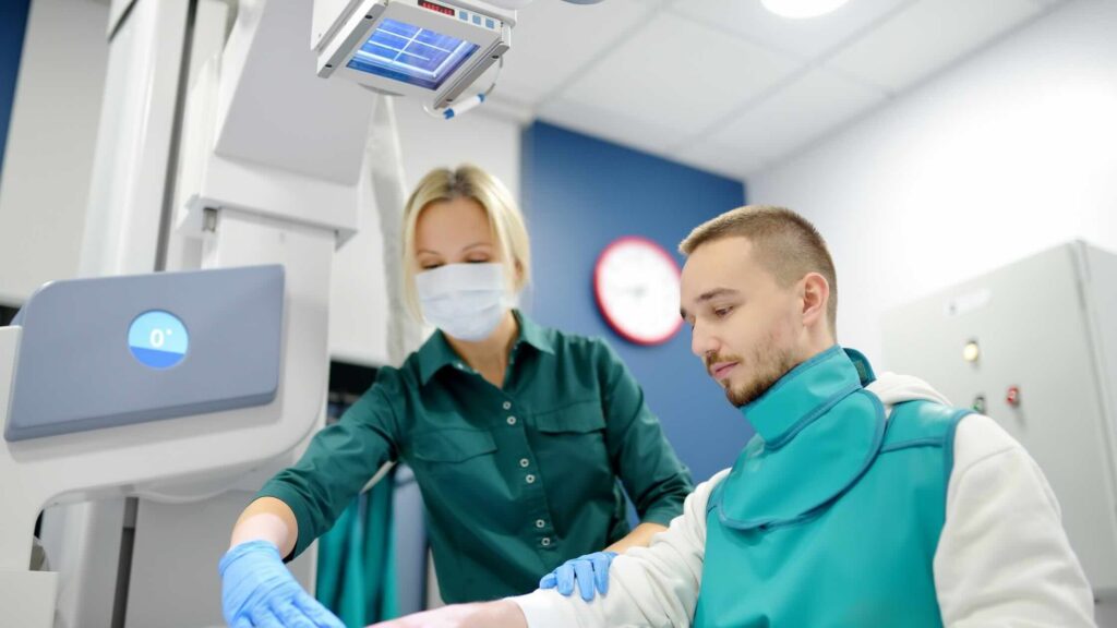 A radiologic technologist positions a patient wearing a lead apron before an X-ray.