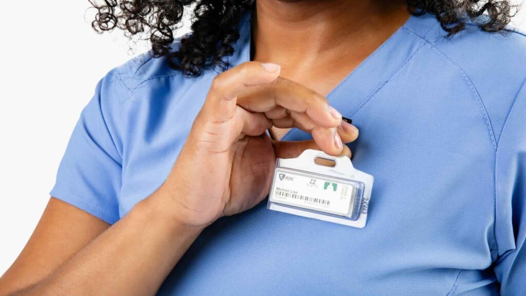 A woman clips an OSL dosimeter to her light blue scrubs.
