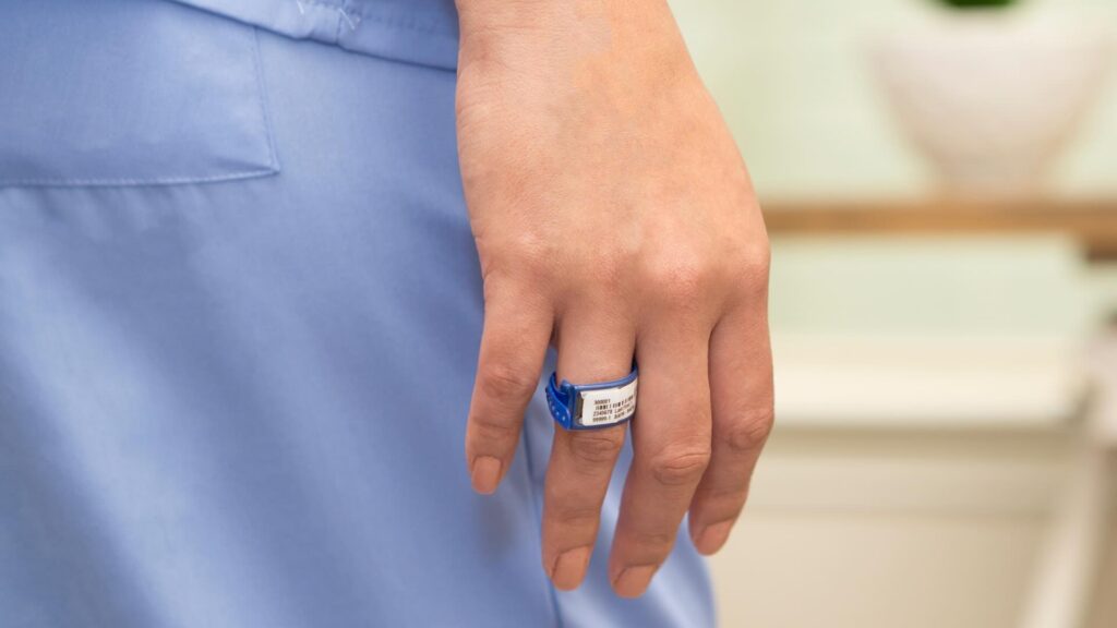 A zoomed in photo of a woman's hip; she wears light blue scrubs with a TLD ring dosimeter on her right ring finger.
