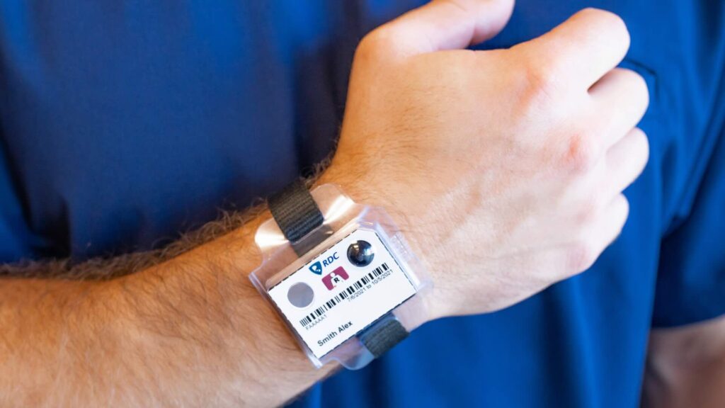 A zoomed in photo of a man in dark blue scrubs wearing a TLD dosimeter on his wrist.