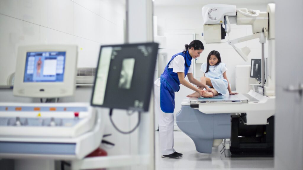 An X-ray technician helps a patient prepare for an imaging session.