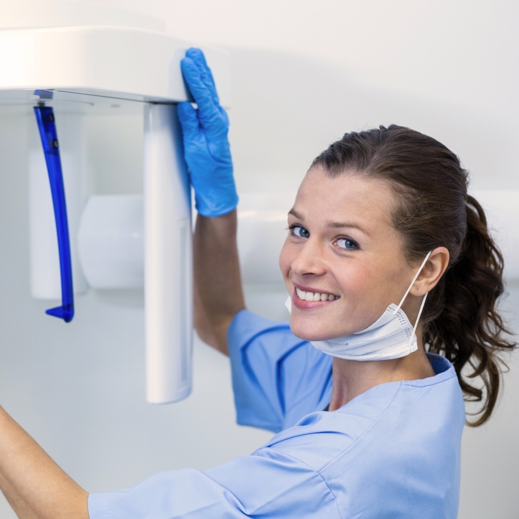 A dental technician poses for a smile near imaging equipment.