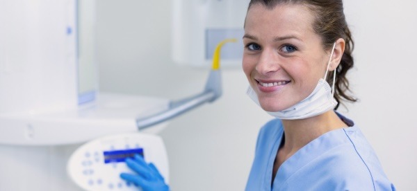 A dental technician poses for a smile near imaging equipment.