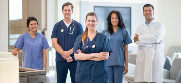 Dental staff pose for a photo while wearing scrubs and a white coat.