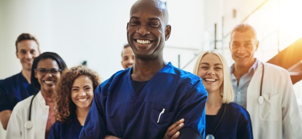 Staff from a healthcare group smile for a photo while wearing scrubs and white coats.