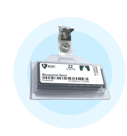 Clear ID badge with clip, labeled RDC and ZZ 5 of 10, featuring a barcode. Name listed as Becquerel Henri. Dates shown are 4/1/2023 to 7/1/2023. Badge is set against a blue circle background.