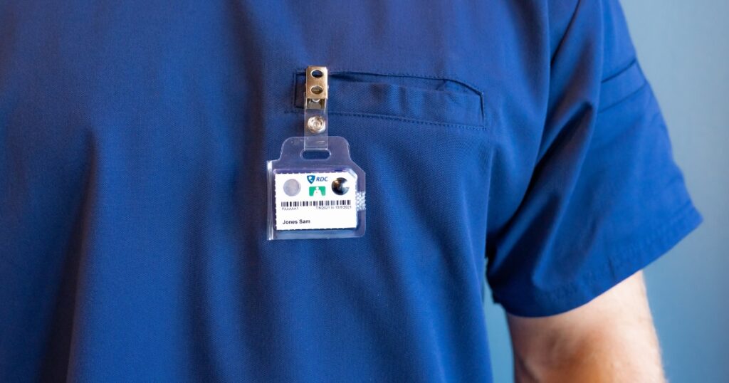 A TLD badge clipped on the front pocket of a nurse wearing dark blue scrubs.