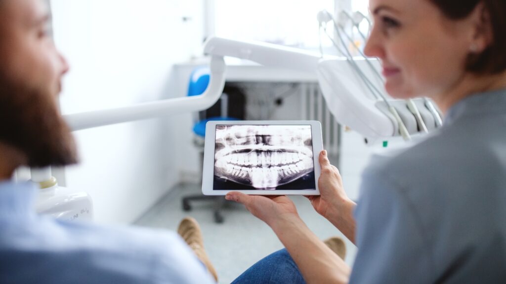 A dentist reviews X-rays with a patient on a tablet.