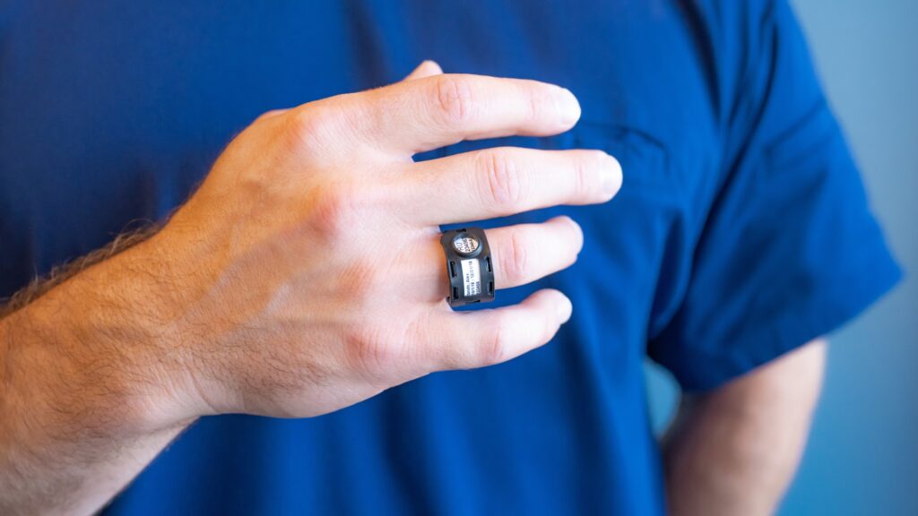 An employee working in nuclear medicine wears a TLD ring badge on his finger for dosimetry monitoring.