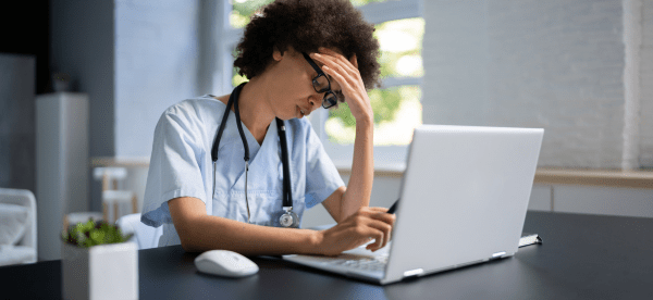 A frustrated healthcare worker struggles while on hold during a live chat.