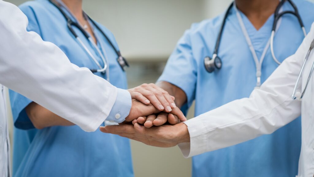 Hospital staff stack hands during a team huddle.