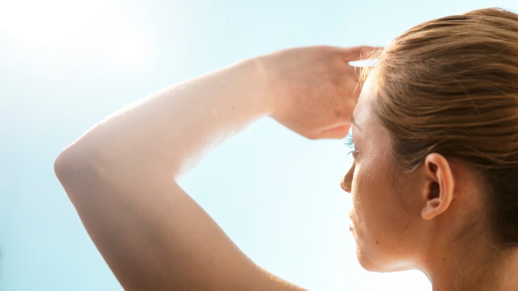 A woman looking at the sky holds her hand in front of her face to shield her eyes.