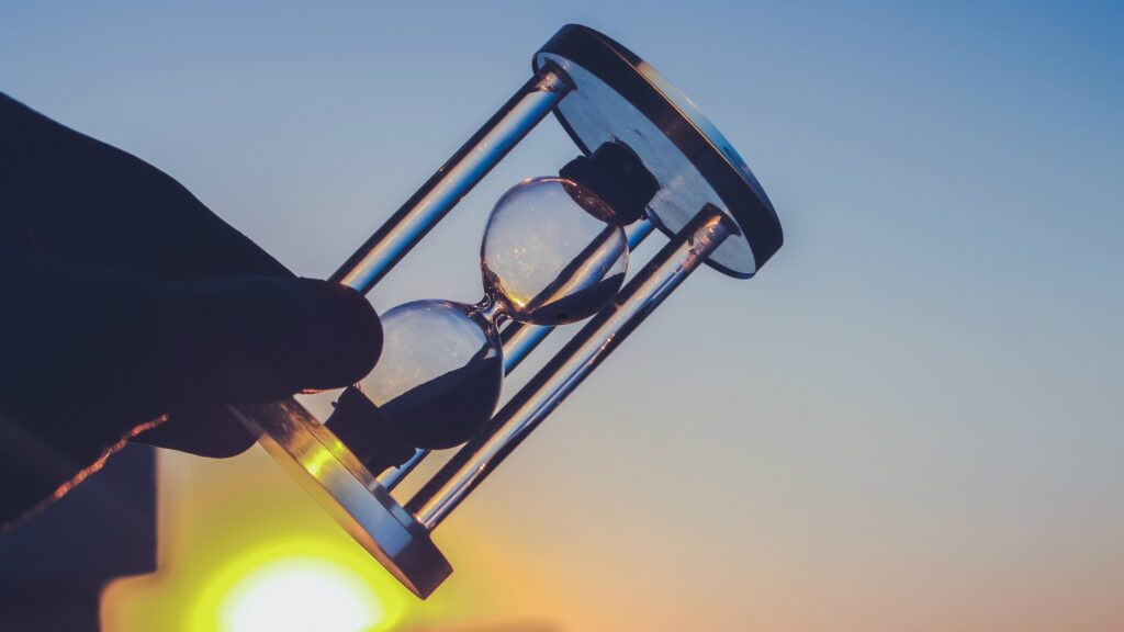 A person holds an hour glass as the sun sets in the background.