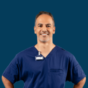 A dental employee smiles while wearing dark blue scrubs.