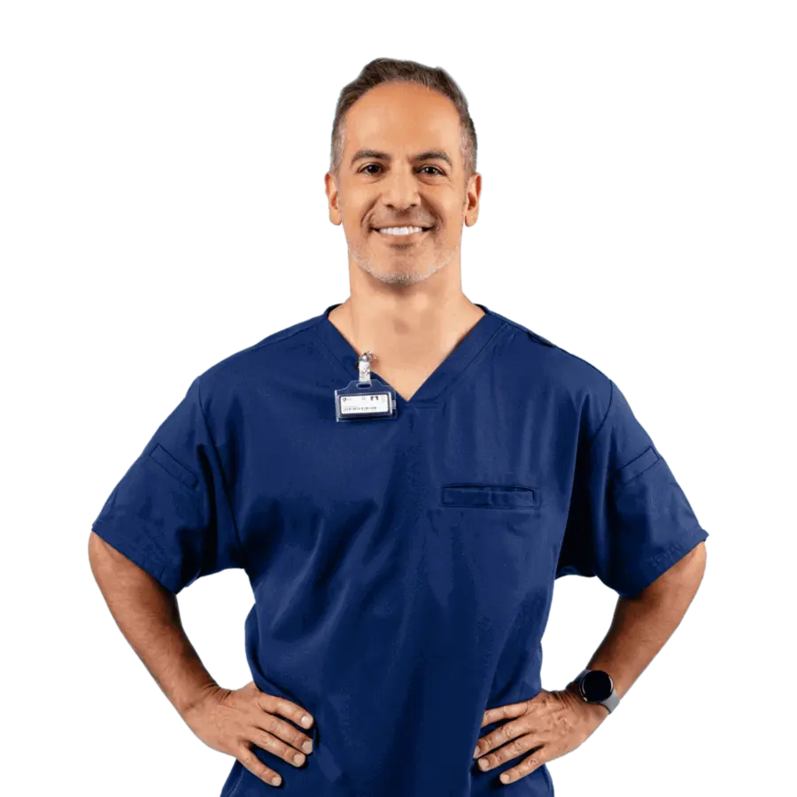 A dental employee wearing dark blue scrubs with his hands on his hips.