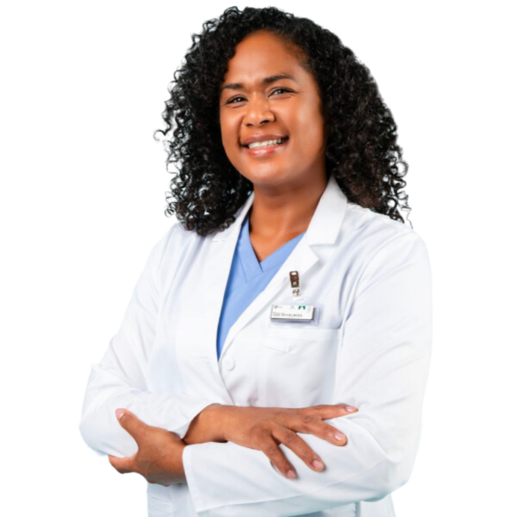 Smiling individual with curly hair wearing a lab coat and a blue medical top, standing confidently with arms crossed.