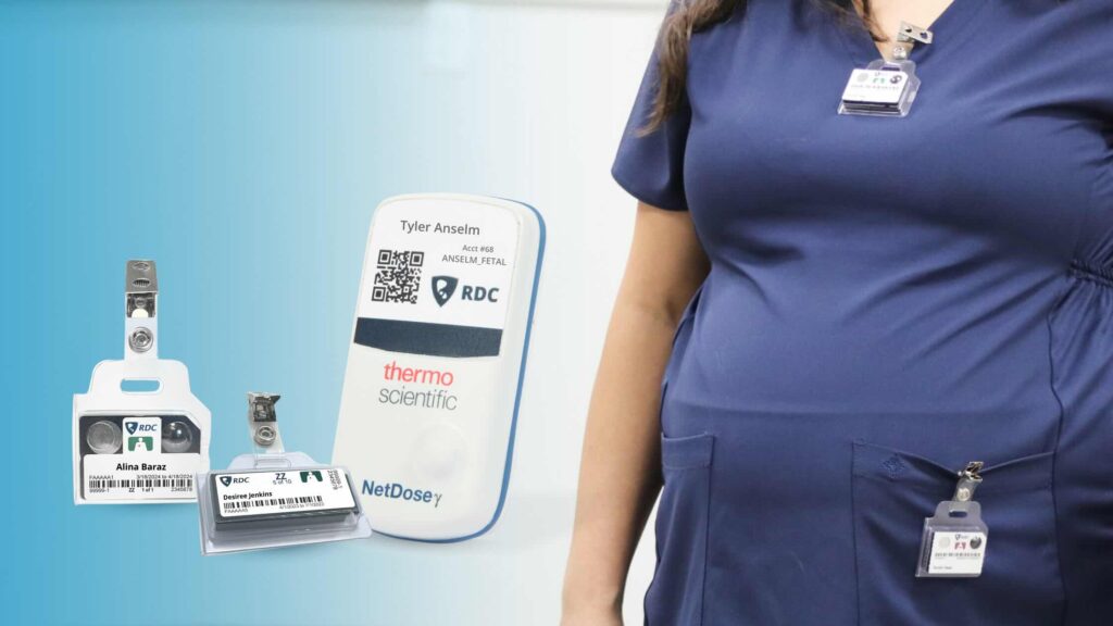 A pregnant healthcare worker in a navy scrubs wears a fetal monitoring badge and a whole body monitoring badge. Three close-up fetal badge solutions are shown on the left against a light blue background.