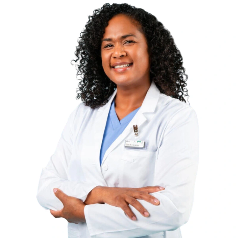 Smiling individual with curly hair wearing a lab coat and a blue medical top, standing confidently with arms crossed.