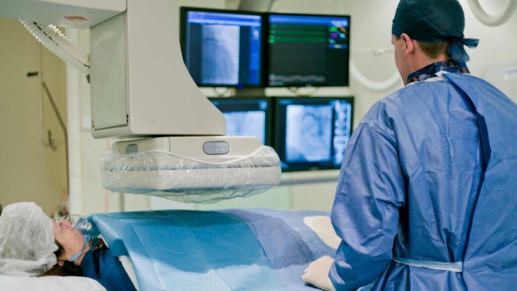 A surgeon prepares a patient for a procedure in a cardiac catheterization laboratory