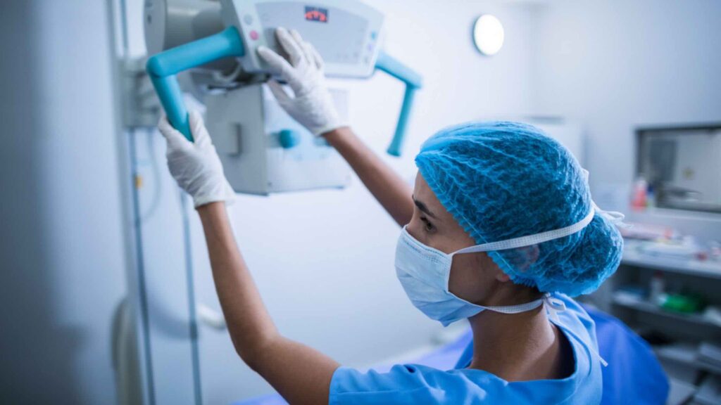 An imaging technologist positions an X-ray machine over a patient in hospital