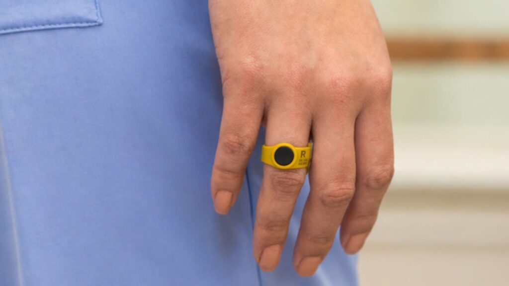 A zoomed in photo of a woman's hip; she wears light blue scrubs with an OSL ring dosimeter on her right ring finger.
