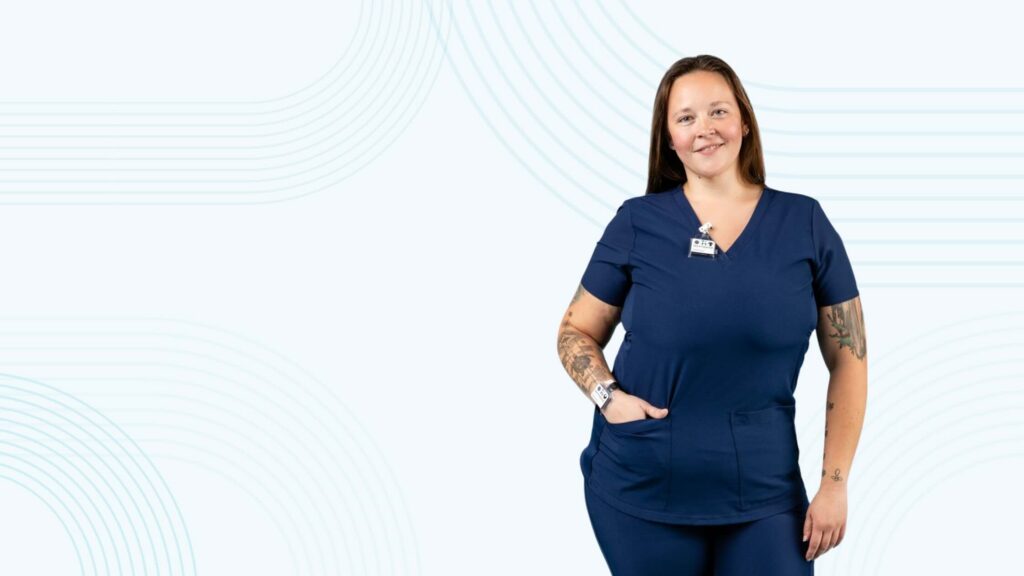 A smiling employee wears a TLD dosimeter badge clipped to dark blue scrubs.