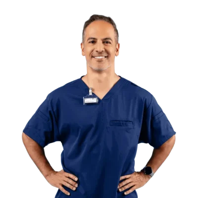 A dental employee wearing dark blue scrubs with his hands on his hips.